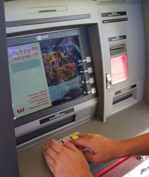 A photo of a person covering the number pad while entering their PIN into an automatic teller machine