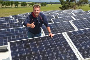 Photo of my brother-in-law standing on a rooftop surrounded by solar panels. He is smiling with pride.