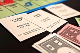 Photo of a monopoly game in progress. One player is not going very well and has had to turn many of his property cards over, indicating that he has mortgaged these back to the bank.