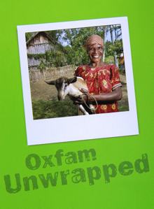 Photo of an African woman in a village. There is a thatched roof house in the background and she is wearing simple clothing, no makeup and no jewelry. She is holding a small goat and looks very happy to have the animal in her arms.