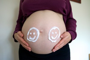 Photo of a pregnant tummy with two smiley faces drawn on it with moisturiser.