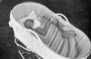 Two photos – the photo on the left is an old black and white showing a baby sleeping in a bassinet. The photo on the right is a modern colour photo showing a newborn baby sleeping in the same bassinet.