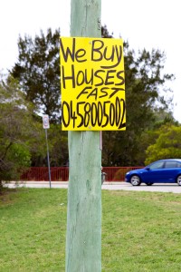 Photo of a sign that reads "We buy houses fast" with a mobile number below.