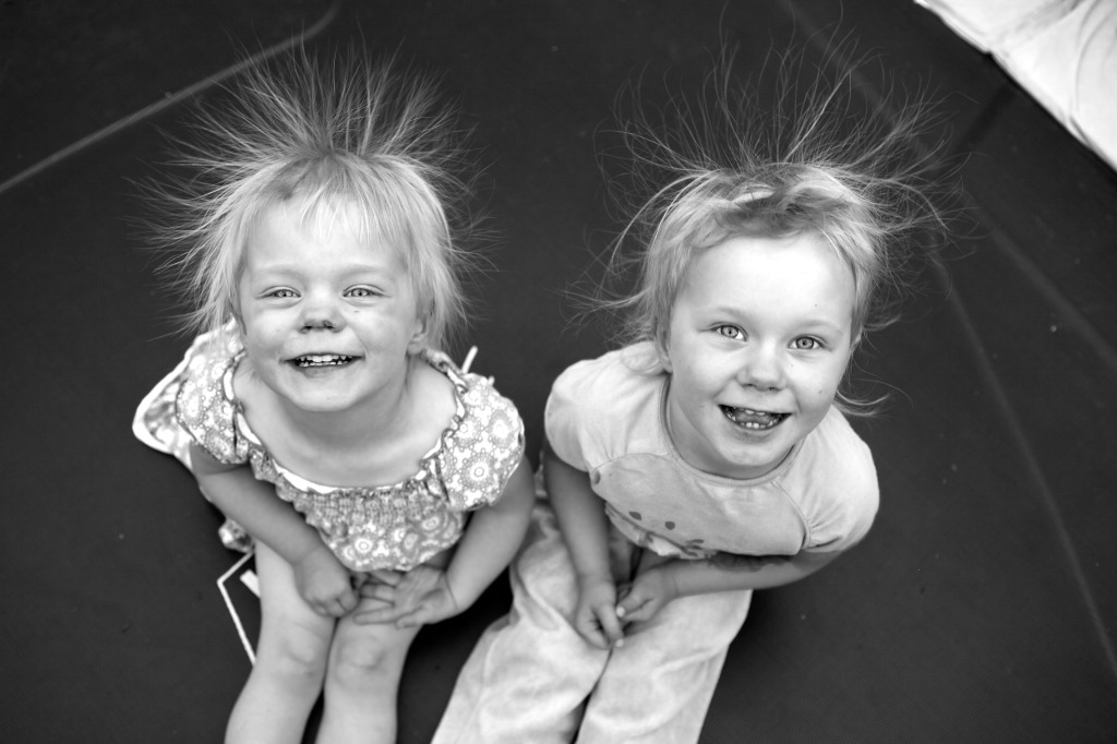 B&W photo of two girls sitting on a trampoline with hair going in all directions due to static electricity.